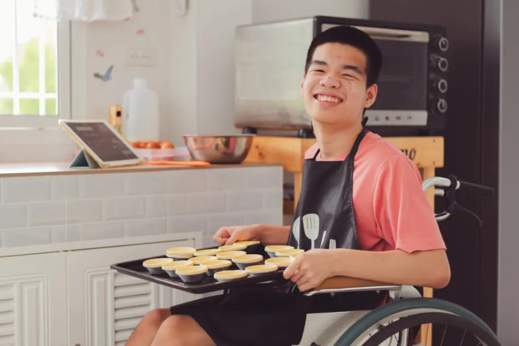 male participant in wheelchair holding a tray of pastry about to go in the oven