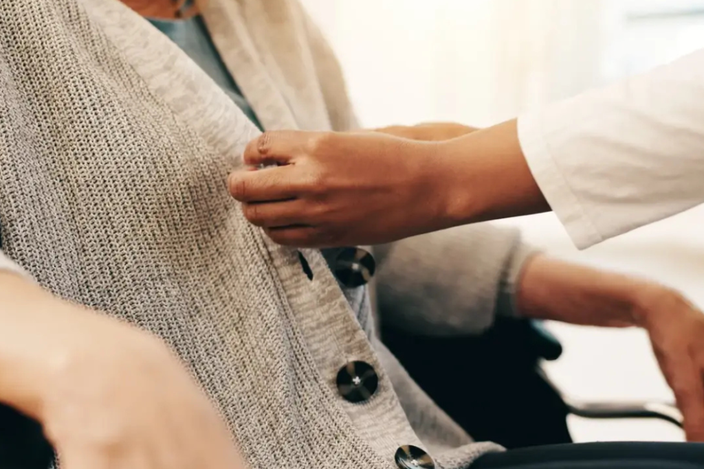 nurse helping woman in wheelchair button up her sweater