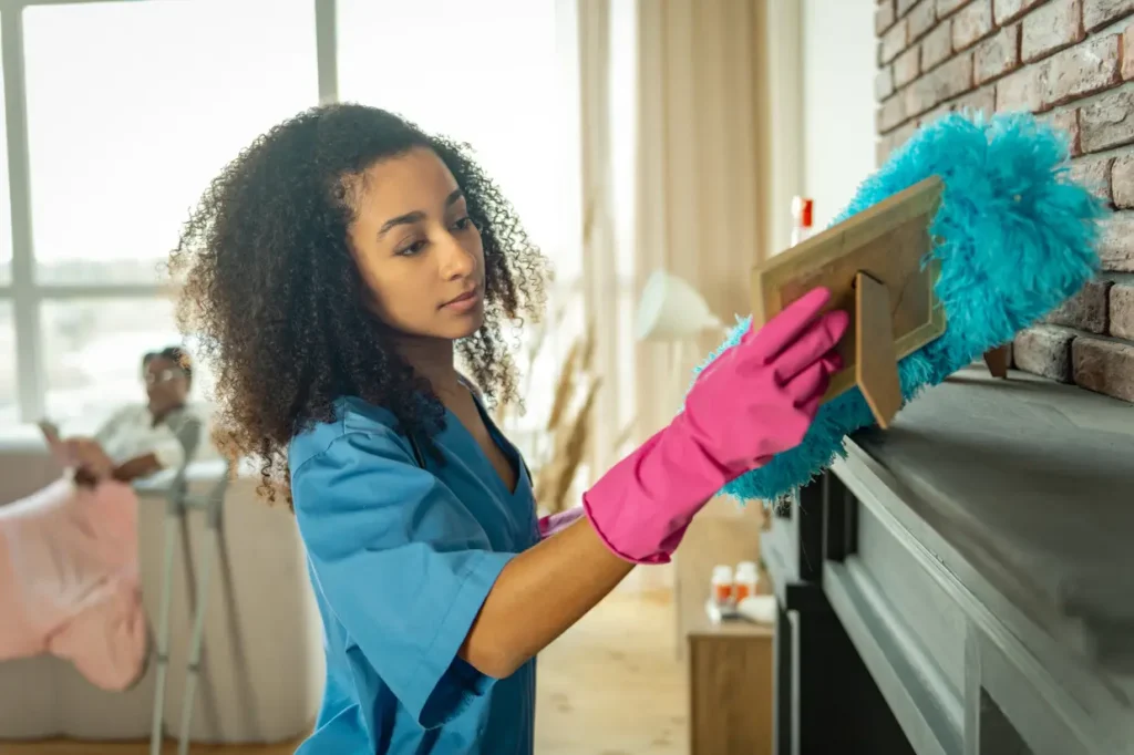 female cleaner dusting a shelf in a participants home