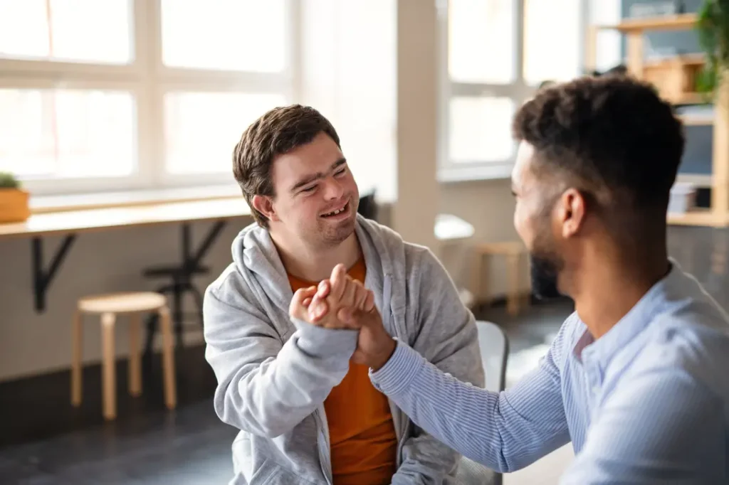 male participant with Down syndrome and his male support worker shaking hands and smiling