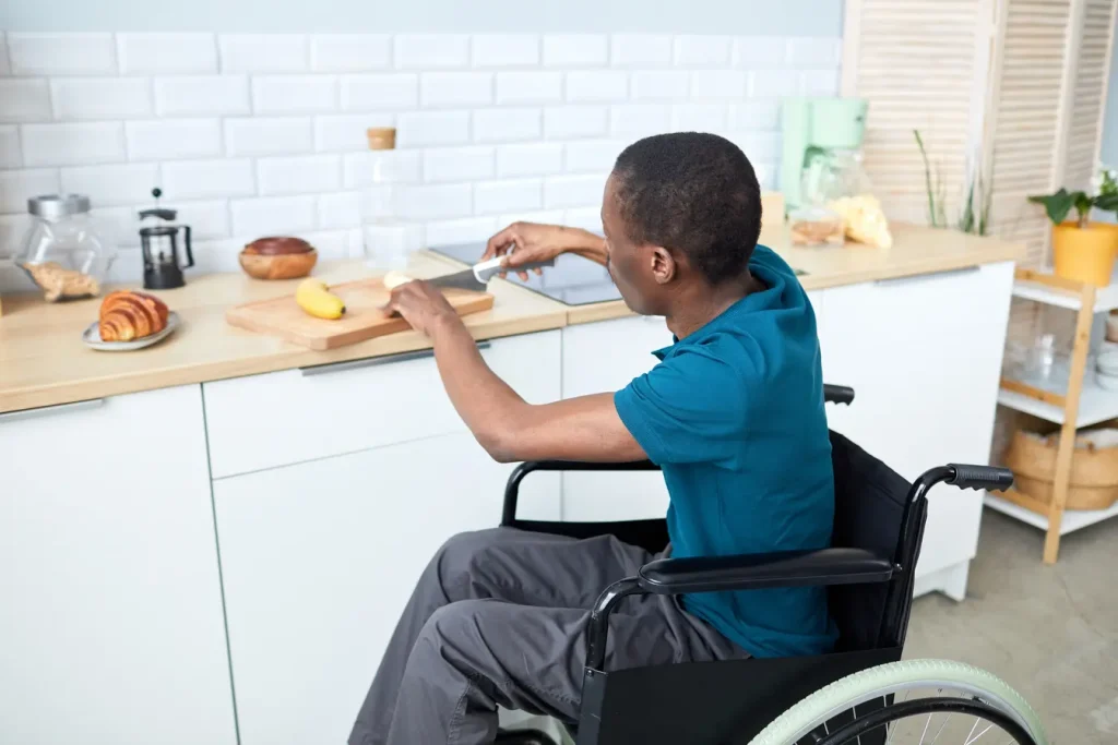 male participant in wheelchair cutting up fruit in the kitchen