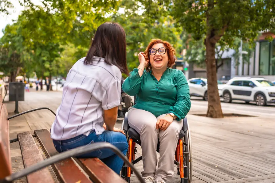 Female participant in wheelchair talking with her support worker on a bench outside